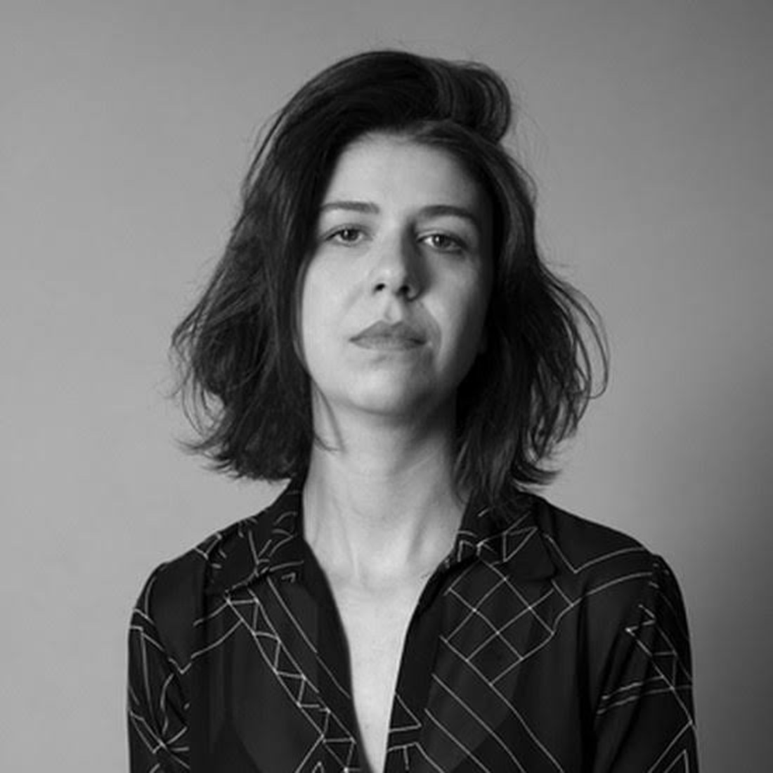 Retrato de Letícia Bassit em preto e branco, de frente para a câmera, com camisa escura estampada